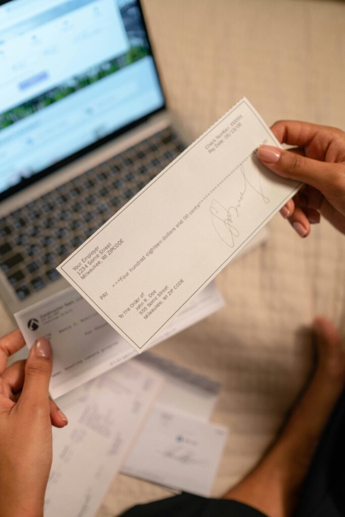 pexels photo 6862457 6862457 Individual holding a cheque over laptop, signifying online banking or financial transaction.